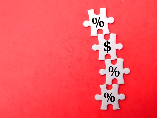 Four white puzzle pieces arranged vertically on a red background. The top piece has a percent symbol, the second piece has a dollar sign, the third piece has a percent symbol, and the bottom piece has a percent symbol.